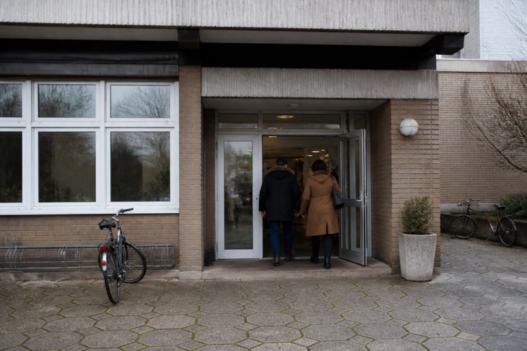 Eingang eines Bildungshauses, zwei Erwachsene betreten das Gebäude